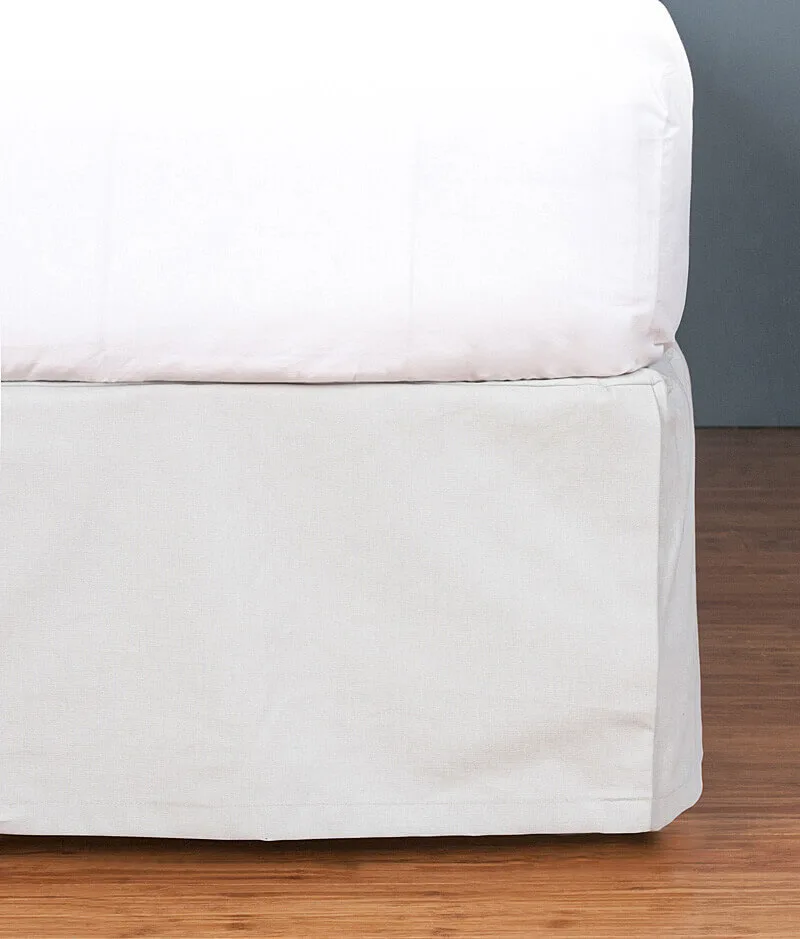 A neatly covered bed with white linens on a wooden floor against a grey wall.