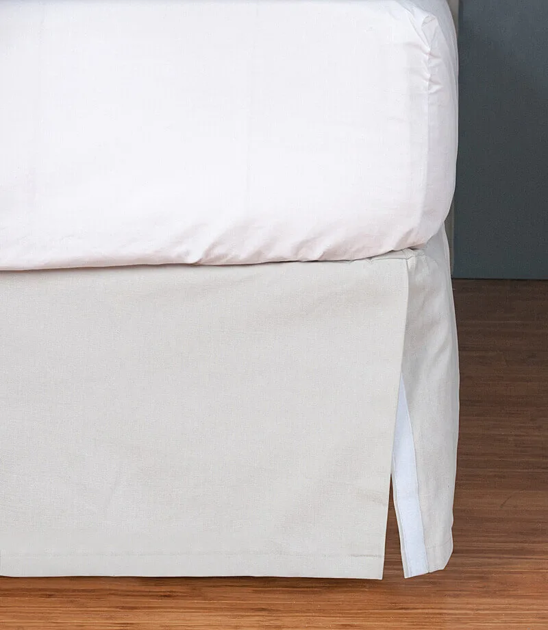 White bed with bed skirt on a wooden floor against a grey wall.