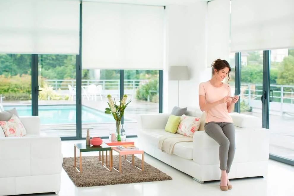 A person standing in a bright, modern living room with a sofa, table, and pool view.